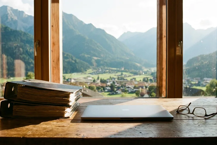 Aktenordner und Laptop auf einem Schreibtisch mit Alpenblick